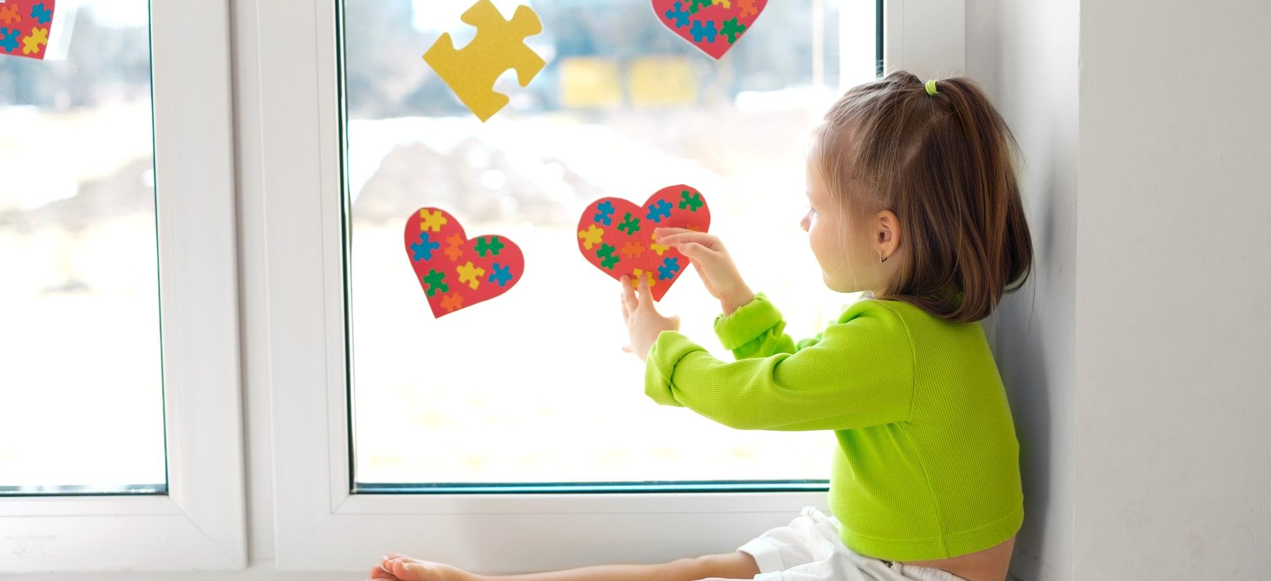 Una niña pega corazones de puzle en una ventana